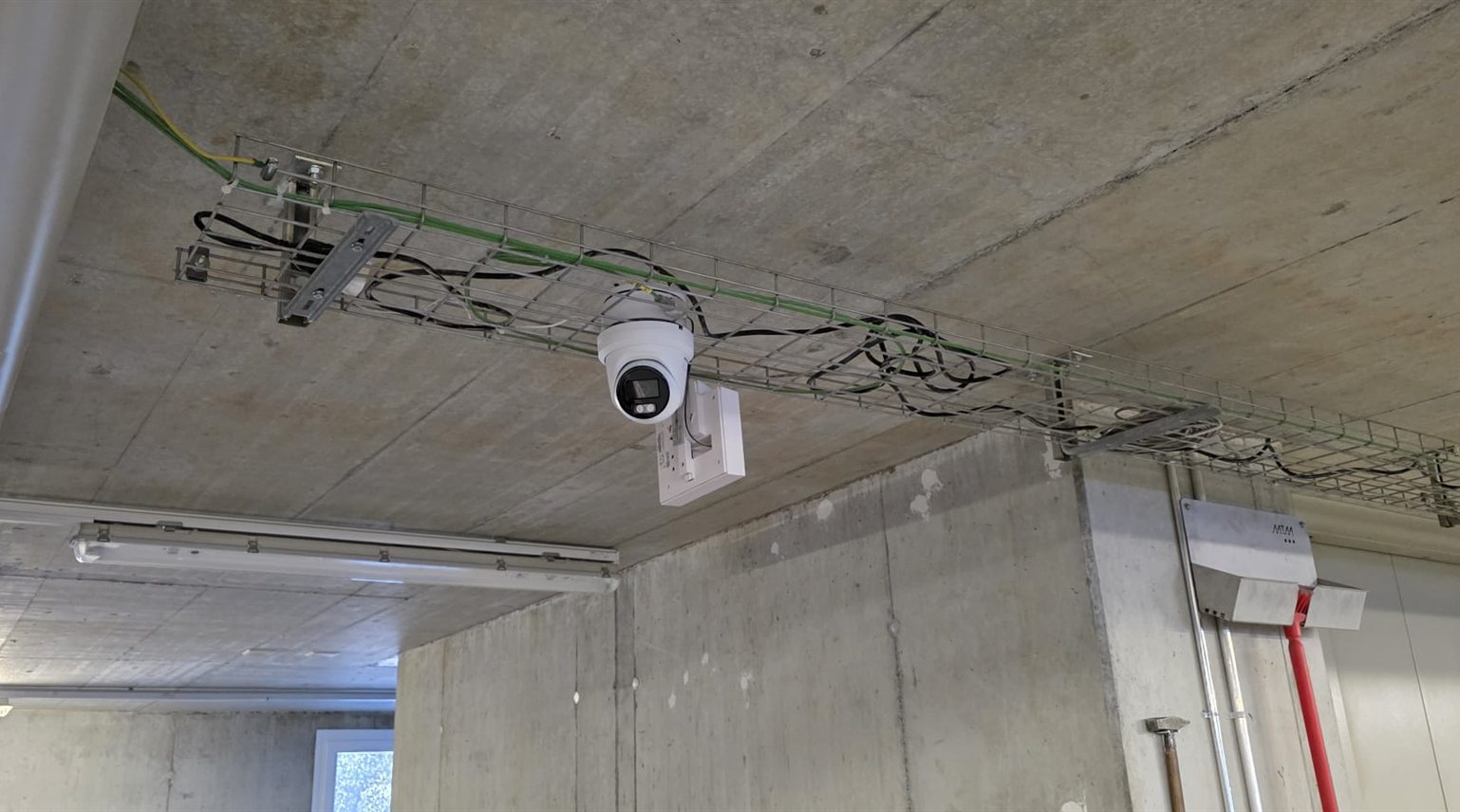 Weisse Hikvision-ColorVu-Turret-Kamera an der Betondecke ueber einer Kabelpritsche im Lager