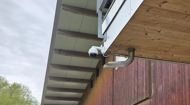 Nahaufnahme der weissen smart-cam Stall-Kamera (PTZ) an ihrer Metall-Halterung unter dem Vordach des Stalls