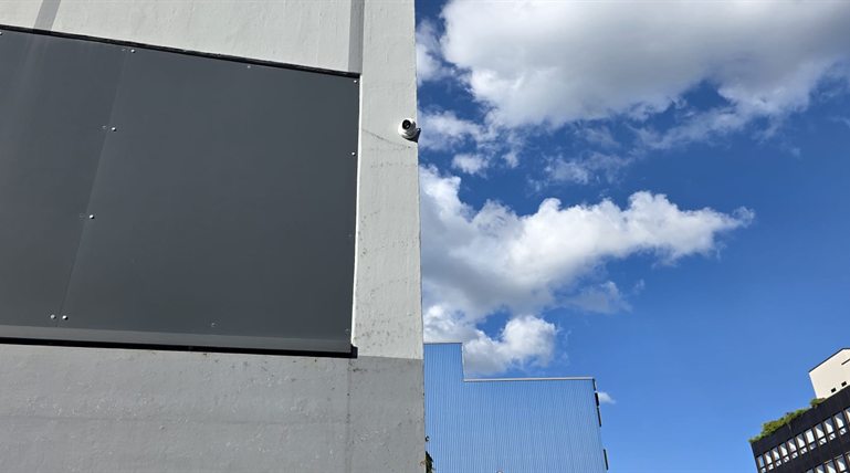 Weisse Turret-Überwachungskamera an der Ecke eines Industriegebäudes vor blauem Himmel