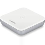 Flacher weisser Bosch Smart Home Wassermelder auf dem Boden neben einer Waschmaschine