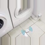 Flacher weisser Bosch Smart Home Wassermelder auf dem Boden neben einer Waschmaschine