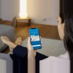 Flacher weisser Bosch Smart Home Wassermelder auf dem Boden neben einer Waschmaschine