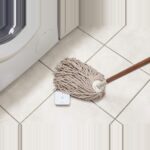 Flacher weisser Bosch Smart Home Wassermelder auf dem Boden neben einer Waschmaschine