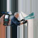 Mann misst eine Innenwand mit dem Laser-Entfernungsmesser