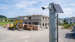 Ueberwachungskamera mit Solarpanel hoch an einem Stahlmast auf einer aufgeraeumten Baustelle