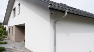 Kleine unauffaellige Kamera hoch an der Ecke eines modernen Wohnhauses unter der Dachkante