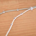 Zwei weisse Kabel mit Nagelschellen auf einer Holzflaeche befestigt