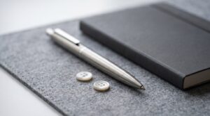 Kugelschreiber und zwei Hemdknoepfe auf einer Schreibunterlage neben einem Notizbuch
