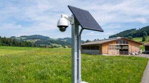 Ueberwachungskamera mit Solarpanel fachgerecht an einem Stahlmast am Rand einer gepflegten Wiese montiert