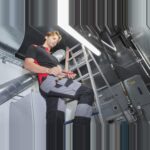 Elektriker auf einer Leiter arbeitet mit dem Schraubendreher in einem Technikraum
