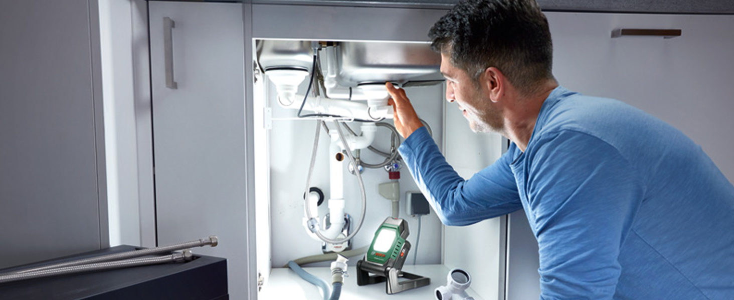 Grün-schwarze Bosch Akku-Arbeitsleuchte UniversalWorkLight 18V-2100 mit LED-Lichtfeld, aufgeklapptem Standbügel und Tragegriff, daneben der grüne Verkaufskarton – Detail 1