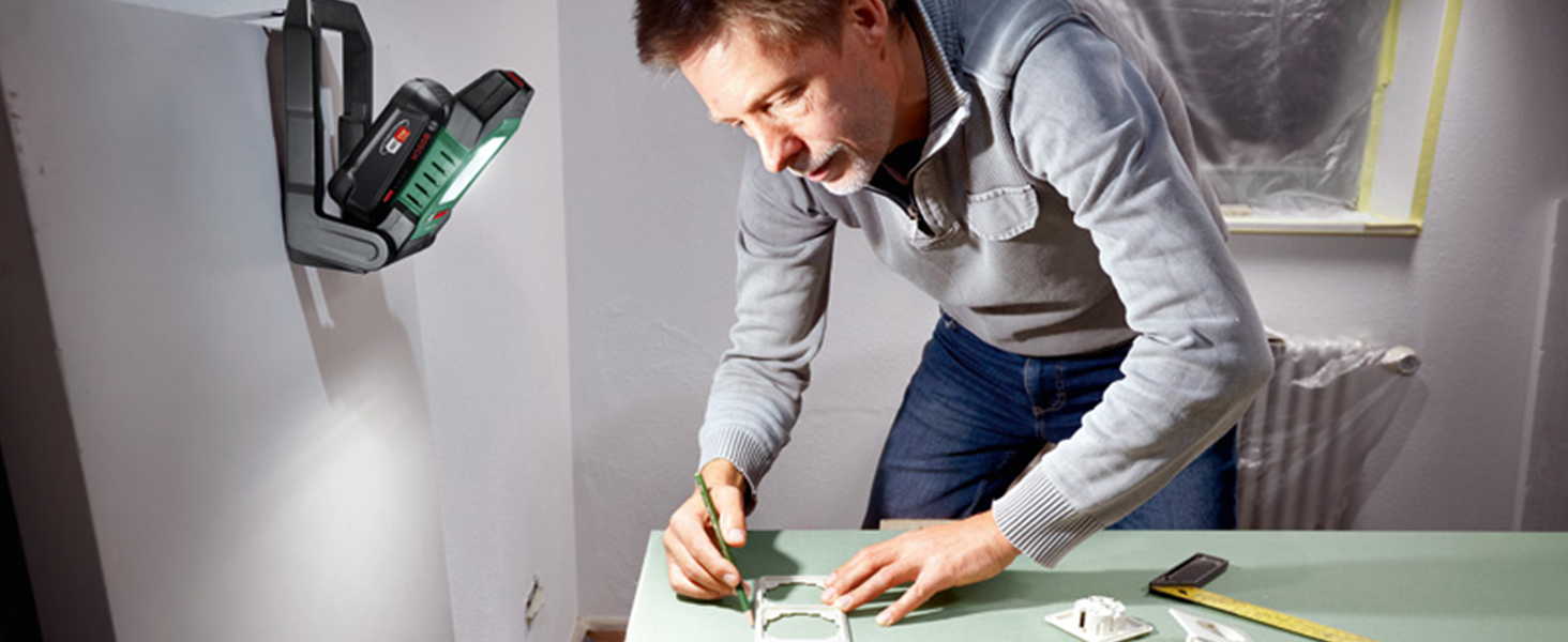 Grün-schwarze Bosch Akku-Arbeitsleuchte UniversalWorkLight 18V-2100 mit LED-Lichtfeld, aufgeklapptem Standbügel und Tragegriff, daneben der grüne Verkaufskarton – Detail 2