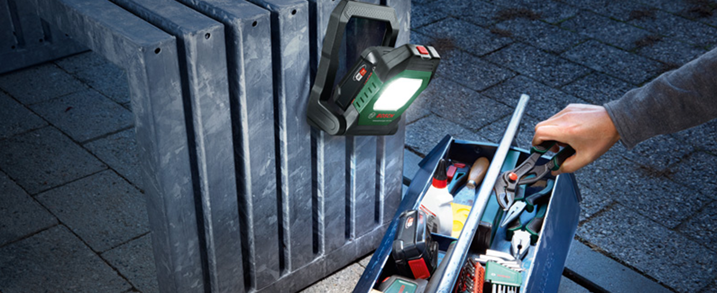 Grün-schwarze Bosch Akku-Arbeitsleuchte UniversalWorkLight 18V-2100 mit LED-Lichtfeld, aufgeklapptem Standbügel und Tragegriff, daneben der grüne Verkaufskarton – Detail 3