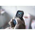 Schwarz-blauer Bosch Professional Laser-Entfernungsmesser GLM 50-23 G mit Farbdisplay, daneben Gürteltasche, Trageschlaufe und zwei AA-Batterien