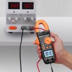 Orange-schwarze Proster Stromzange mit beleuchtetem LCD, geöffneten Messbacken, Messleitungen, Krokodilklemmen und Aufbewahrungstasche