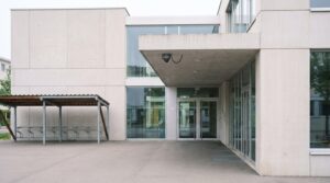 Sicherheitskamera unter dem Dachvorsprung am Eingang eines Schweizer Schulhauses