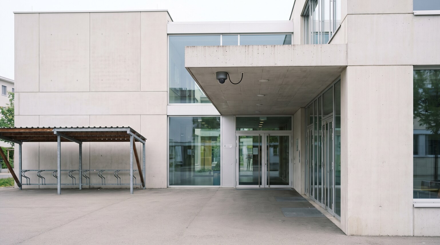 Sicherheitskamera unter dem Dachvorsprung am Eingang eines Schweizer Schulhauses