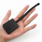 Mini-Kamera im Kompaktgehäuse mit Objektiv an Flachkabel in der Hand